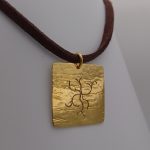 Notre pendentif, modèle branches sauvages carré, en plaqué or, avec un cordon marron.